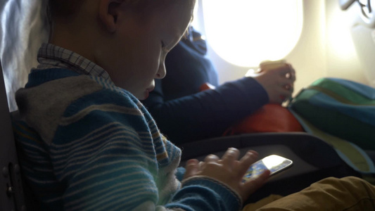 小男孩坐在飞机上玩智能手机视频