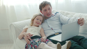 父亲和女儿躺在沙发上拿着笔记本电脑6秒视频