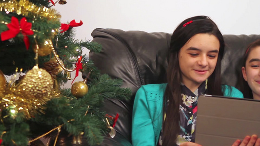 年轻的快乐女孩在圣诞树旁用平板电脑在线交谈视频