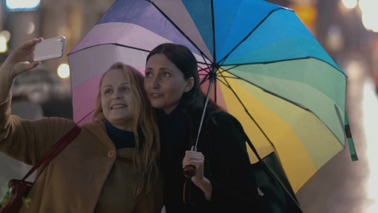 雨天打着五彩雨伞的年轻女子和她的母亲在街上自拍视频