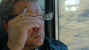 坐火车旅行时戴眼镜的老人透过窗户看着远处的风景然后他摘下眼镜16秒视频