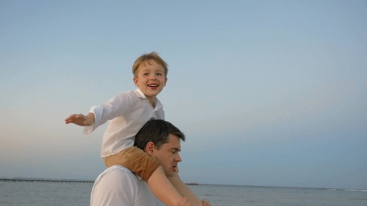 在海边快乐的小男孩坐在父亲的肩膀上模仿飞机飞行视频