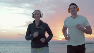 年轻夫妇戴着耳机在日出时沿着大海一边听着音乐一边奔跑17秒视频