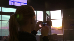 机场年轻女子用智能手机通过窗户拍摄日落照片14秒视频
