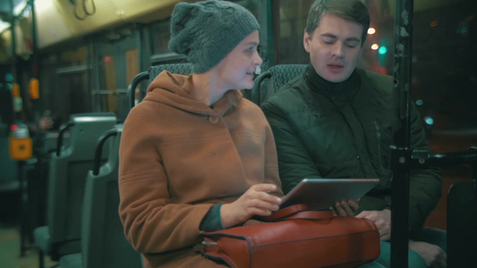 年轻人和女人在傍晚的城市乘公共汽车他们在使用平板电脑交谈视频