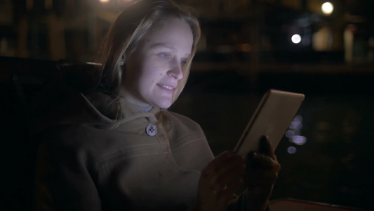 夜晚年轻的女人坐在船上玩手机视频