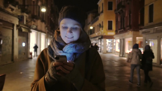 冬天的夜晚女孩拿着手机在街上走视频