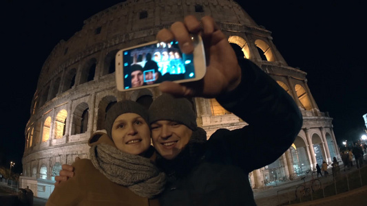 快乐的年轻夫妇夜晚在古罗马斗兽场旅游用手机自拍的特写视频