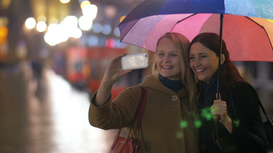 两个女性朋友夜晚漫步在雨天的城市用手机自拍视频