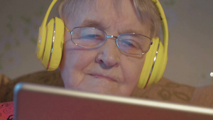 一位戴眼镜的老年妇女用数字平板电脑和无线耳机在听音乐17秒视频