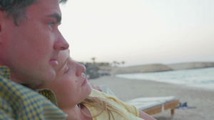 一家三口相拥躺在沙滩的躺椅上夫妇看着远方的风景而儿子在玩智能手机18秒视频