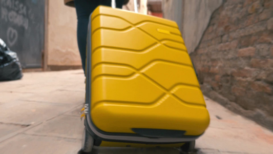 一名女子在狭窄街道上拉动着一个黄色的行李箱视频