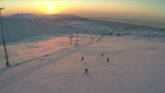 空中拍摄滑雪和滑雪板在滑雪胜地的斜坡与日出的背景视频