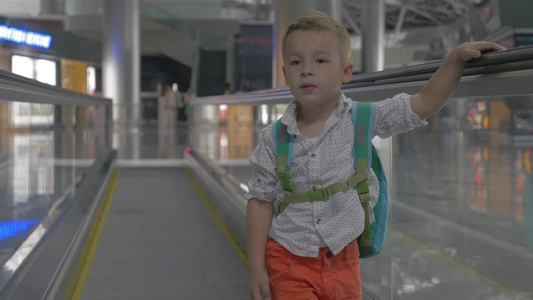 可爱的小男孩背着包在机场的人行通道上做鬼脸视频