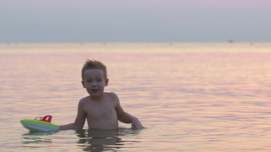 日落时在平静的大海玩玩具船的小男孩视频