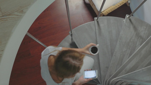 高角度拍摄的年轻女人坐在螺旋楼梯上手里拿着智能手机喝着咖啡44秒视频