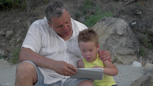 祖父陪小孙子花在户外玩平板电脑视频