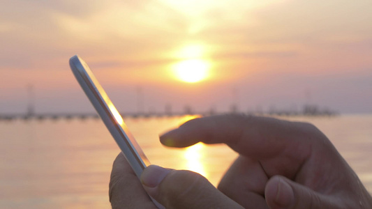 日落在海上男子手里拿着智能手机特写镜头视频