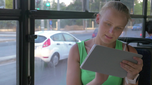 年轻女人坐在公共汽车上使用平板电脑视频