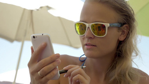 年轻微笑的金发女人在炎热的海滩玩手机19秒视频