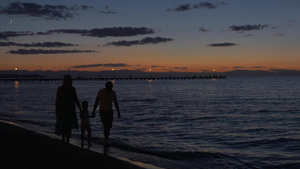 母亲父亲和儿子牵着手赤脚在黄昏中沿着海边散步18秒视频