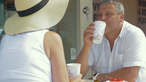 特写老年成年男子和妇女坐在咖啡馆户外喝咖啡吃甜点交谈45秒视频