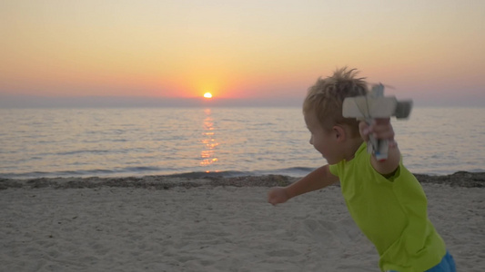日落时分的海边一个小男孩拿着飞机玩具跑向他的父母然后妈妈张开双臂抱起了男孩视频