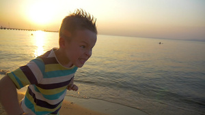 一个穿着条纹T恤的男孩在海边跑步之前做鬼脸6秒视频