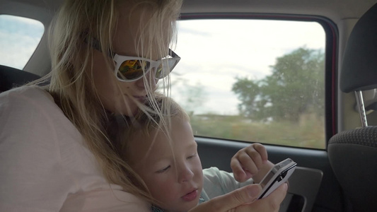 户外旅行时在汽车后座上的小男孩使用母亲的智能手机视频