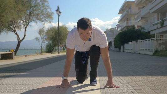 慢动作Steadicam拍摄的一个年轻人从蹲开始跑步，沿着海边慢跑。 每天锻炼以保持健康视频