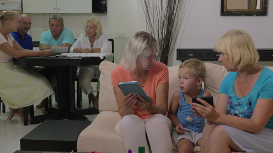 一名妇女在手机上给孩子看东西另一名妇女使用平板电脑视频