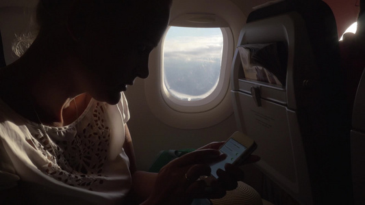 年轻女子在飞机飞行中使用智能手机视频