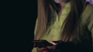 在户外年轻漂亮女人在夜间模糊的灯光背景下使用智能手机上发短信22秒视频