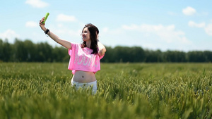 穿着短裤的年轻女人在绿色麦田里用手机自拍15秒视频