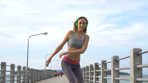 戴着亮绿色耳机听音乐的年轻金发美女在海边的码头上玩滑板17秒视频