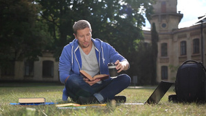 年轻学生坐在校园草坪的绿色草地上读一本书做一些笔记11秒视频