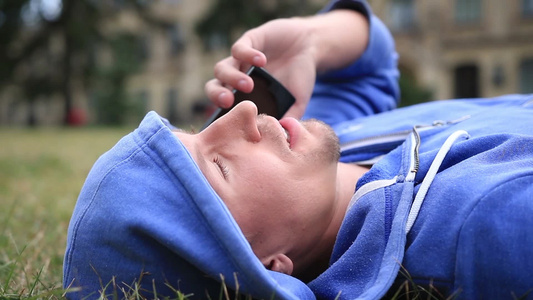 学生躺在校园草坪上和同学用手机交谈视频