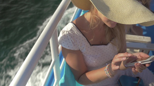 年轻的女人戴着草帽和太阳镜坐在快速行驶的游船上玩着智能手机17秒视频
