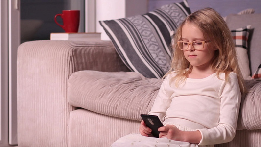 可爱的小女孩坐在沙发附近的地板上玩手机视频