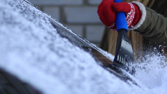 在冬天的早晨戴着手套的女人在汽车挡风玻璃上铲雪视频