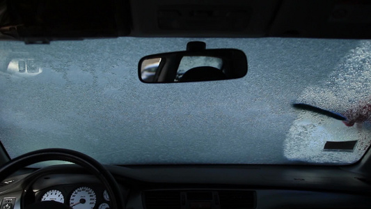  年轻的女司机用蓝色雪刷清扫玻璃上的雪视频