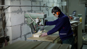 在车间木匠戴着护目镜和耳罩用立式钻床在木板上钻孔23秒视频