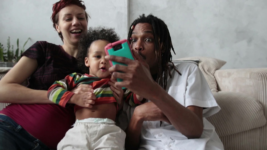 混合种族家庭的男女和蹒跚学步的儿子用手机自拍视频
