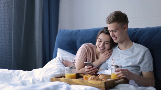年轻的夫妇在床上享用早餐浏览网络视频