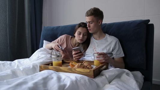 年轻迷人的夫妇在床上看视频内容视频