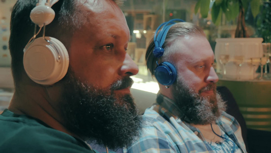 两个留着胡子的男人在贸易中心的沙发用耳机听音乐视频