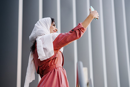 年轻的阿拉伯女人戴着头巾,户外用智能手机拍照阿拉伯女人戴着头巾,用智能手机自拍图片