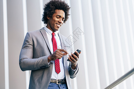 微笑的黑人商人办公楼附近用他的智能手机有AFRO头发的男人黑人商人办公楼附近用智能手机图片