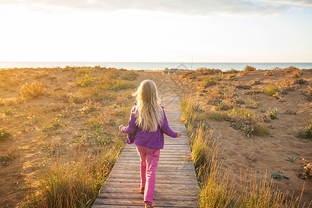 小女孩日出时经过海边的木板路图片