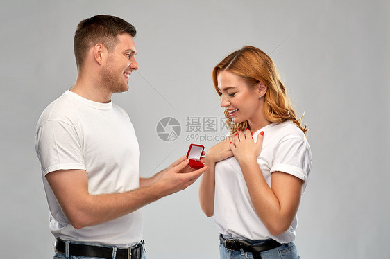 爱情,夫妻,求婚人的男人小红盒子里给灰色背景下快乐的女人钻石订婚戒指男人情人节给女人订婚戒指图片